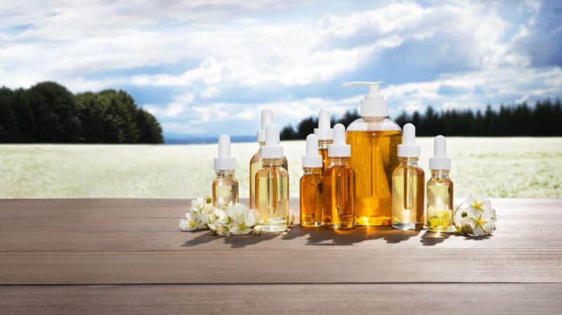 Natural Plant Products meadowfoam seed oil, abyssinian oil, and daikon seed oil bottles displayed on wooden table with white meadowfoam flowers against Oregon Willamette Valley farm background, natural skincare ingredients for oil cleanser and gentle makeup removal