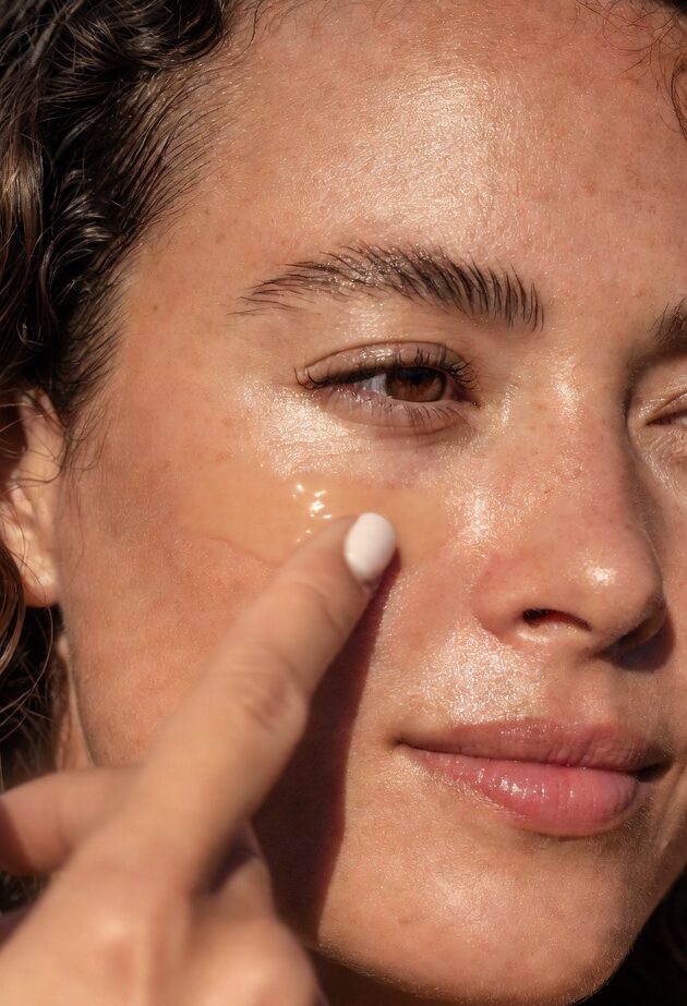 Woman with glowing hydrated skin and shiny hair applying meadowfoam seed oil, natural non-greasy moisturizer for scalp health and dry hair