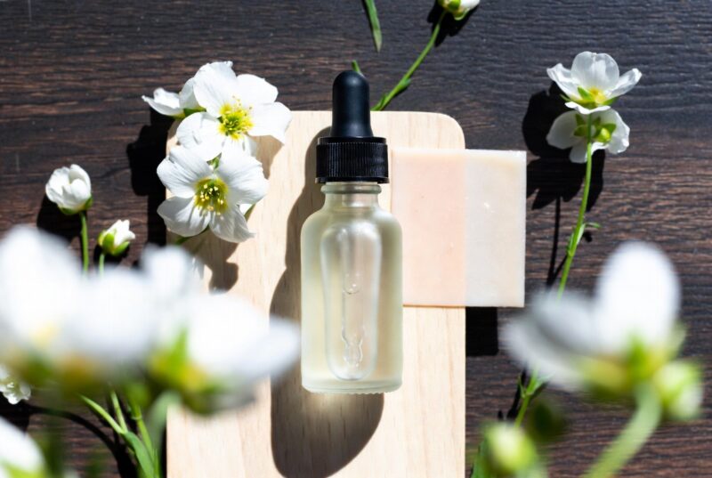 Glass dropper bottle of natural Meadowfoam Seed Oil with white flowers and soap on wooden board, Oregon botanical moisturizing body oil for glowing skin
