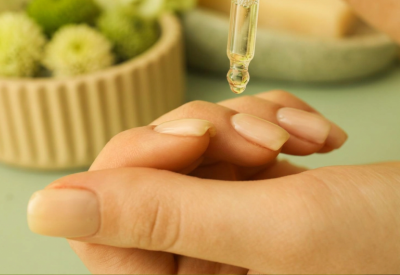 Dropper applying pure natural botanical cuticle oil to clean healthy fingernails, close-up of nourishing nail and cuticle treatment with Oregon grown oils