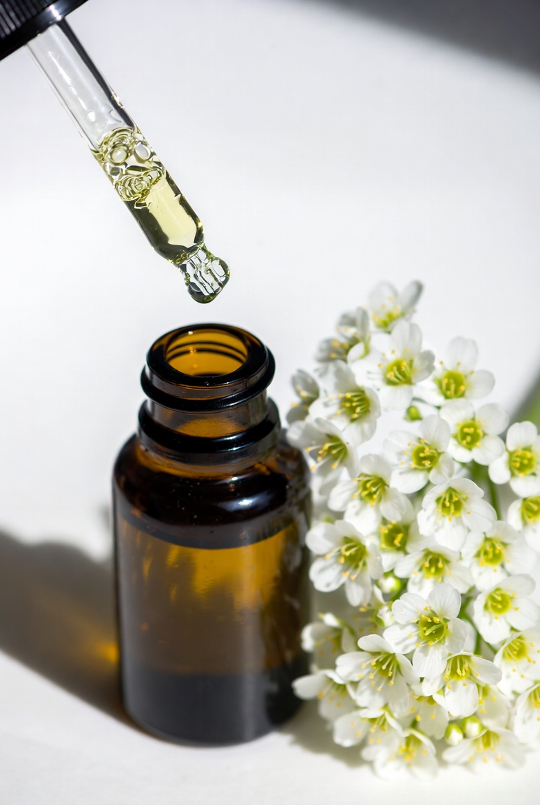 Dark amber glass bottle of pure Oregon meadowfoam seed oil with dropper and fresh meadowfoam flowers, natural botanical oil for hair and skincare