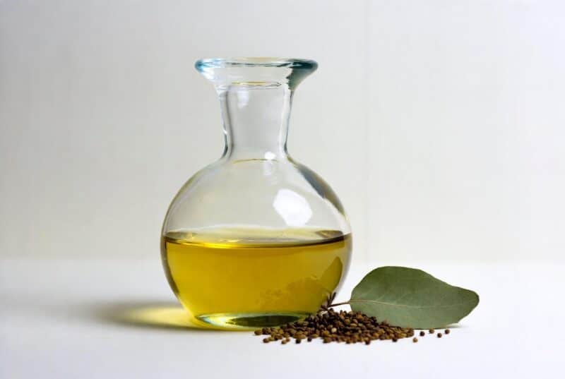 Clear glass bottle of golden meadowfoam or abyssinian oil next to small seeds and green leaf, pure natural plant oil for soft, non-greasy skin hydration