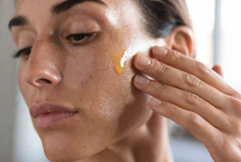 Woman gently applying lightweight natural moisturizer for oily skin using Meadowfoam and Abyssinian oil on her cheek, demonstrating non-greasy absorption for balanced hydrated skin