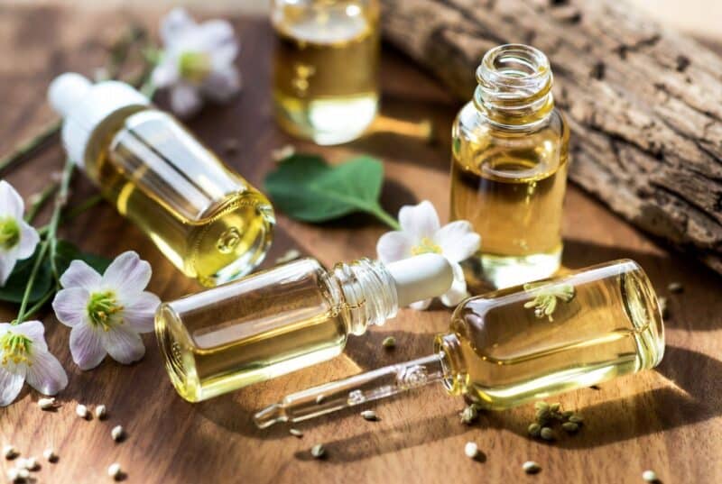 Collection of elegant glass dropper bottles filled with golden natural oils from sustainable skincare brands surrounded by meadowfoam flowers on rustic wood, showcasing high-performance botanical oils for hair and skin hydration