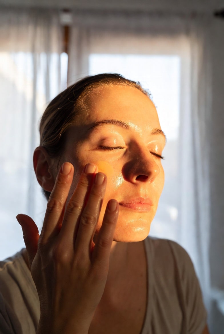 Woman gently applying antioxidant facial oil to glowing skin during morning skincare routine, natural botanical Meadowfoam and Raspberry seed oil benefits