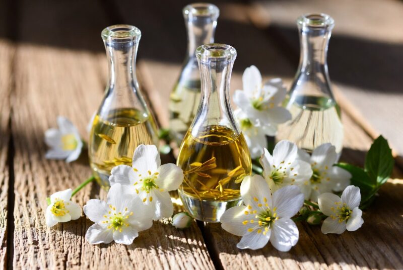 Sustainable body oils in elegant glass bottles with fresh meadowfoam flowers on rustic wood, natural plant-based skincare ingredients from Oregon for deep hydration and skin repair