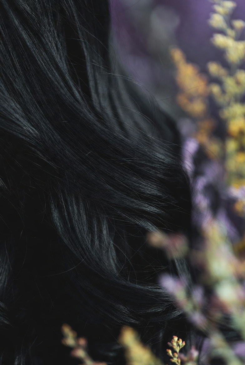 Close-up of smooth silky frizz-free black hair with natural shine, enhanced by Oregon botanical hair oils and meadowfoam flowers, healthy natural hair care results